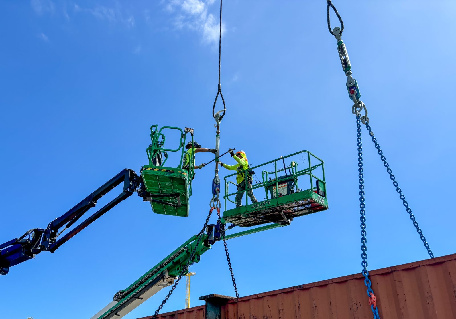 Crew members working from two boom lifts to rig chains above a steel structure
