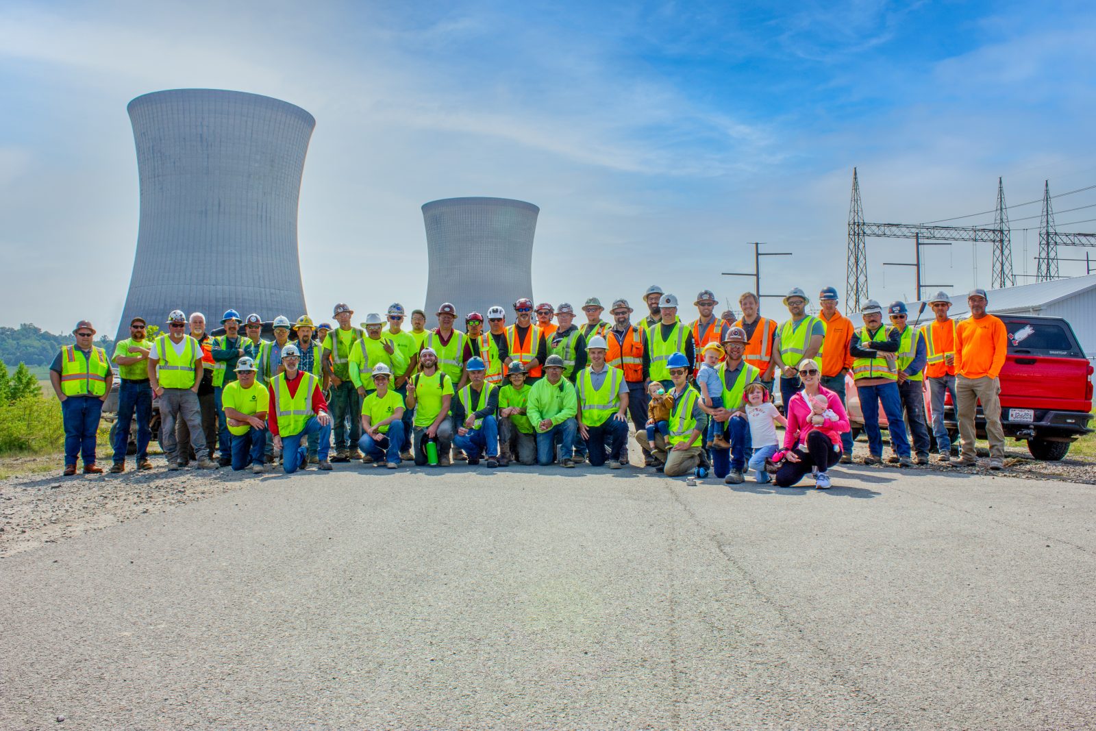 Large group of NADC field and office team members gathered in front of two cooling towers