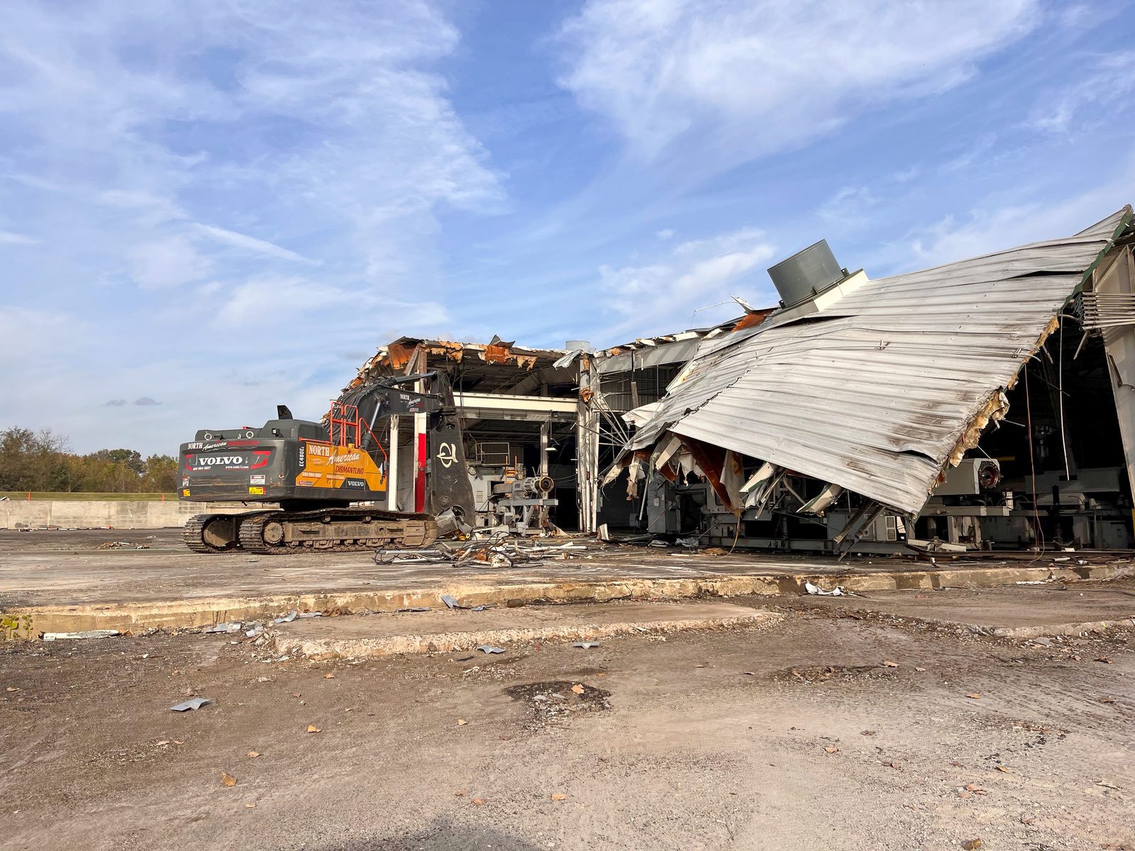 NADC excavator with shear pulling down the steel roof structure of a commercial warehouse building