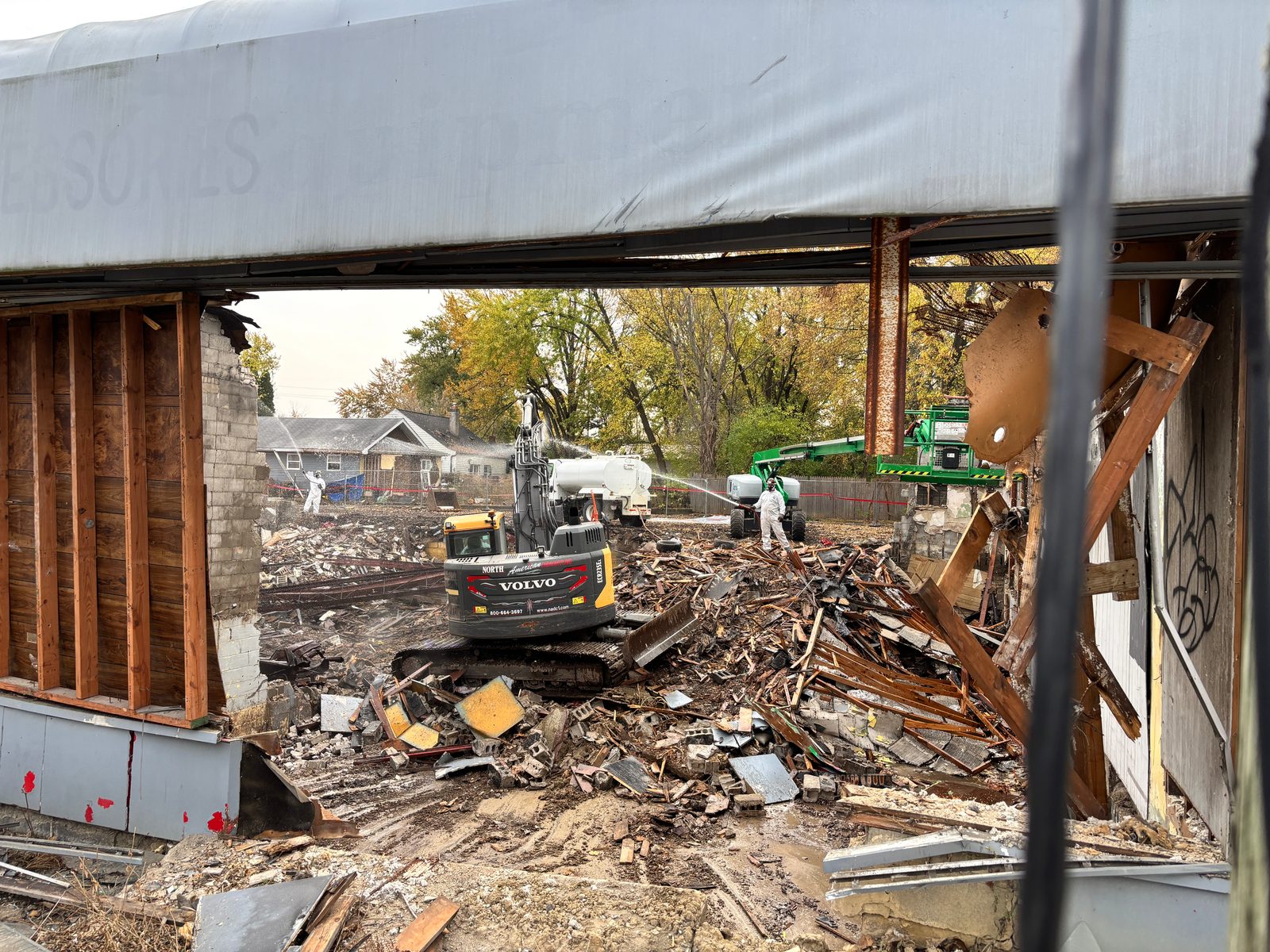 NADC crews wetting down debris while an excavator clears a commercial building along a neighborhood street