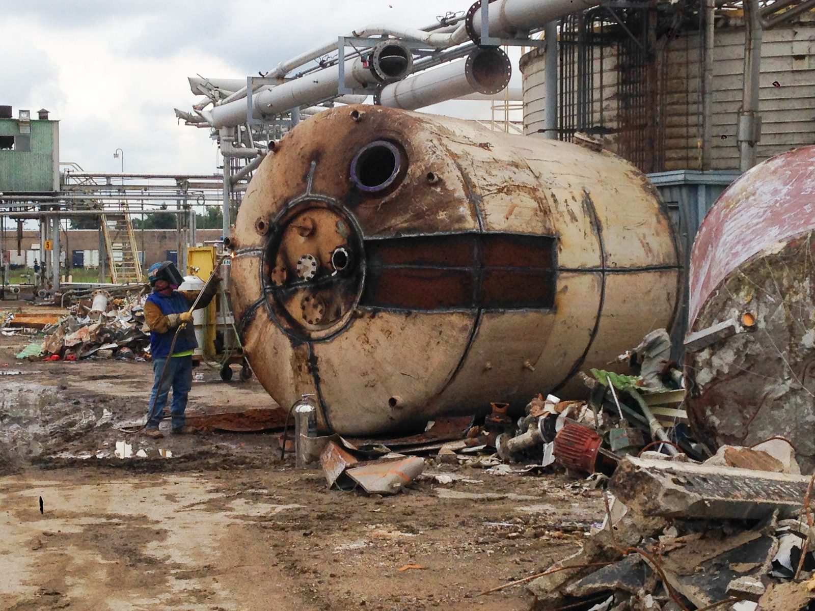 Worker torch-cutting a large process vessel among tank farm structures at the SABIC plant