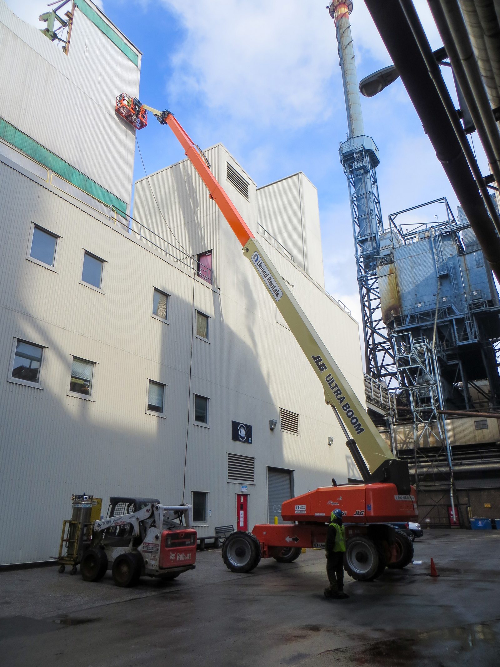 Crew on a boom lift working high on a mill building beside the stack of an operating paper mill