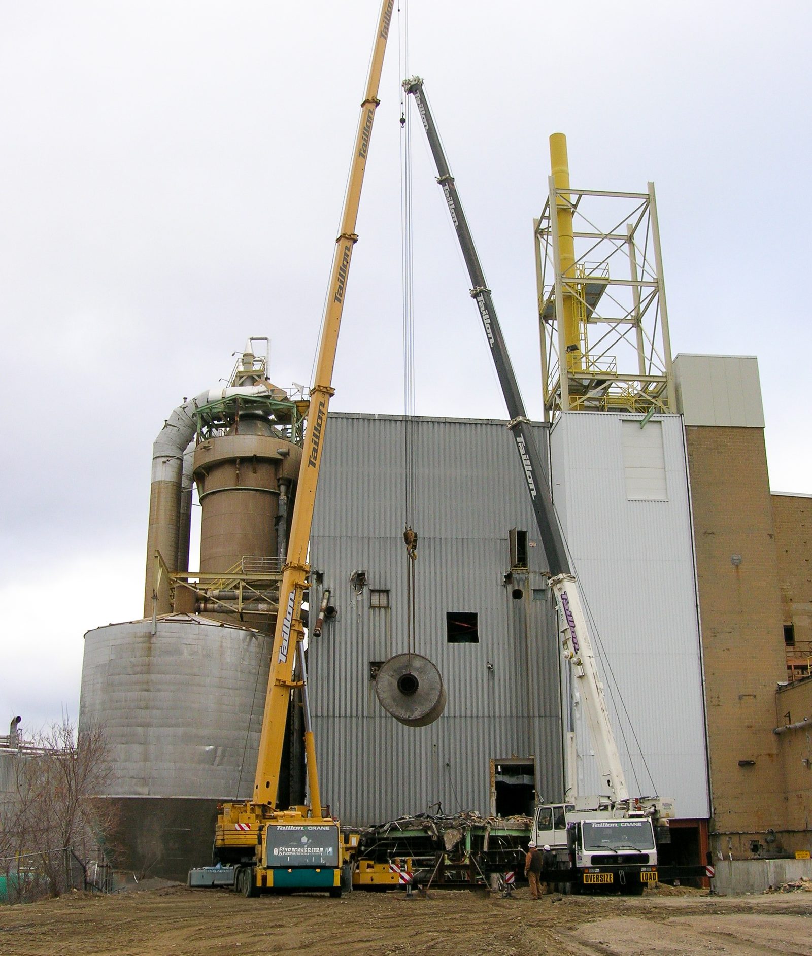 Two cranes rigging equipment out through the wall of a mill building at the Fraser pulp mill