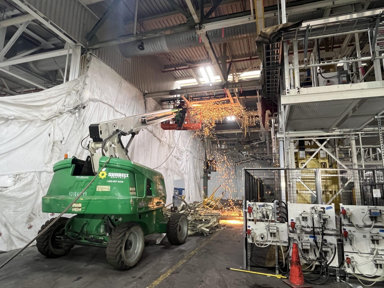 NADC crew torch-cutting overhead conveyor steel from a boom lift inside the Georgetown assembly plant