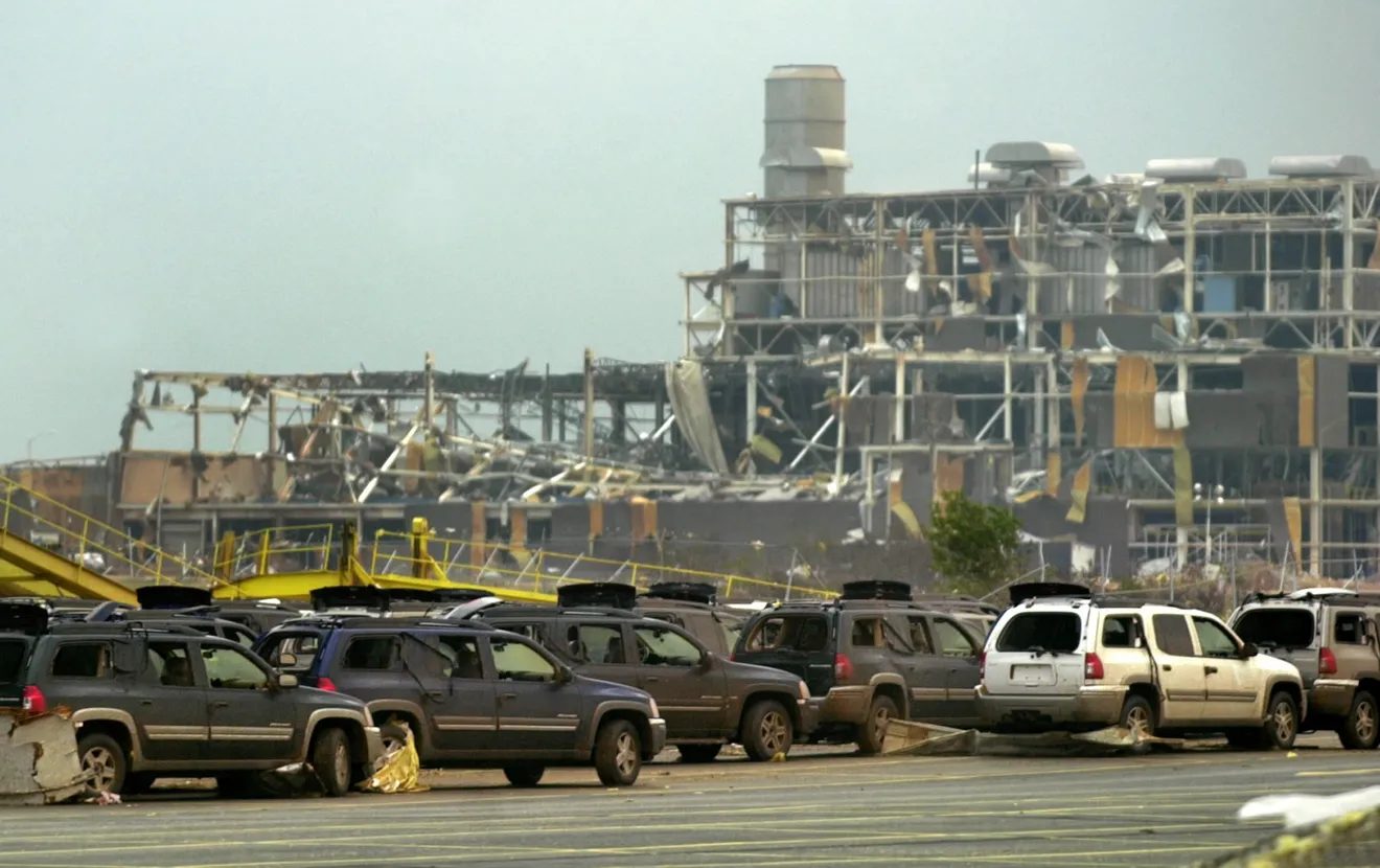 Tornado-damaged structures at the Oklahoma City assembly plant behind storm-damaged vehicles in the parking area