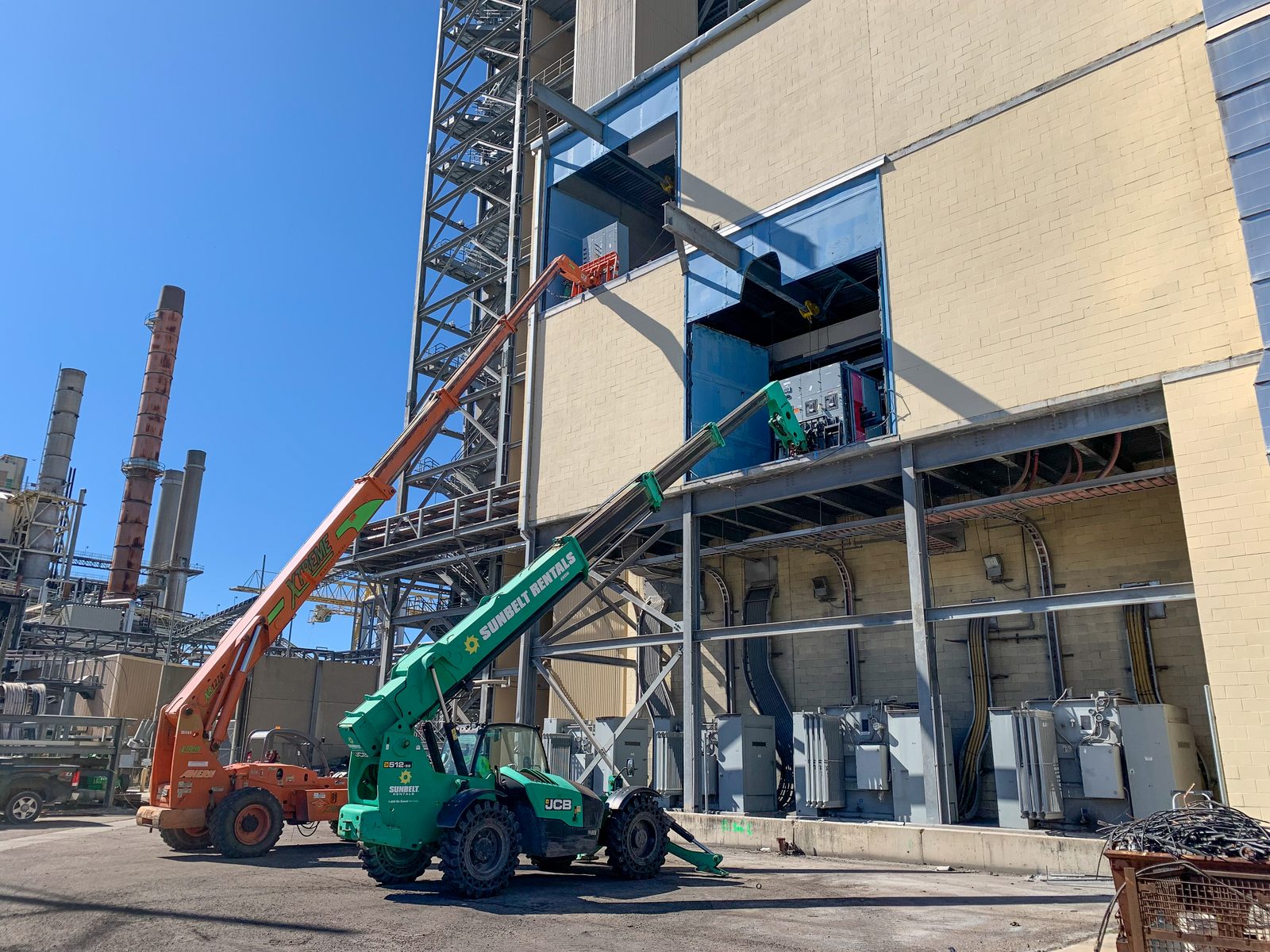 Telehandler and boom lift positioned to remove electrical equipment from the side of an industrial building