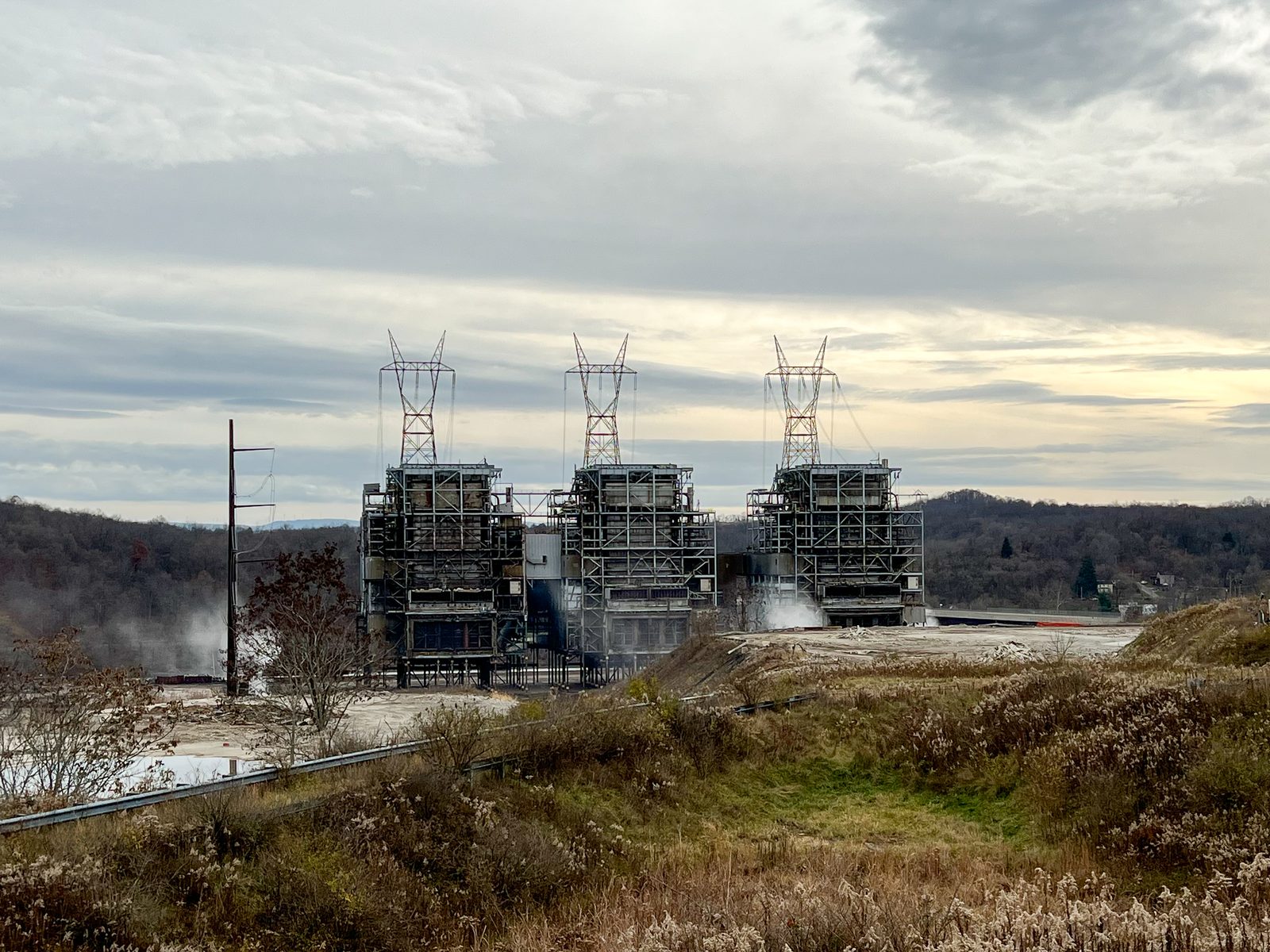 Steel boiler structures at a power plant at dusk beneath transmission lines